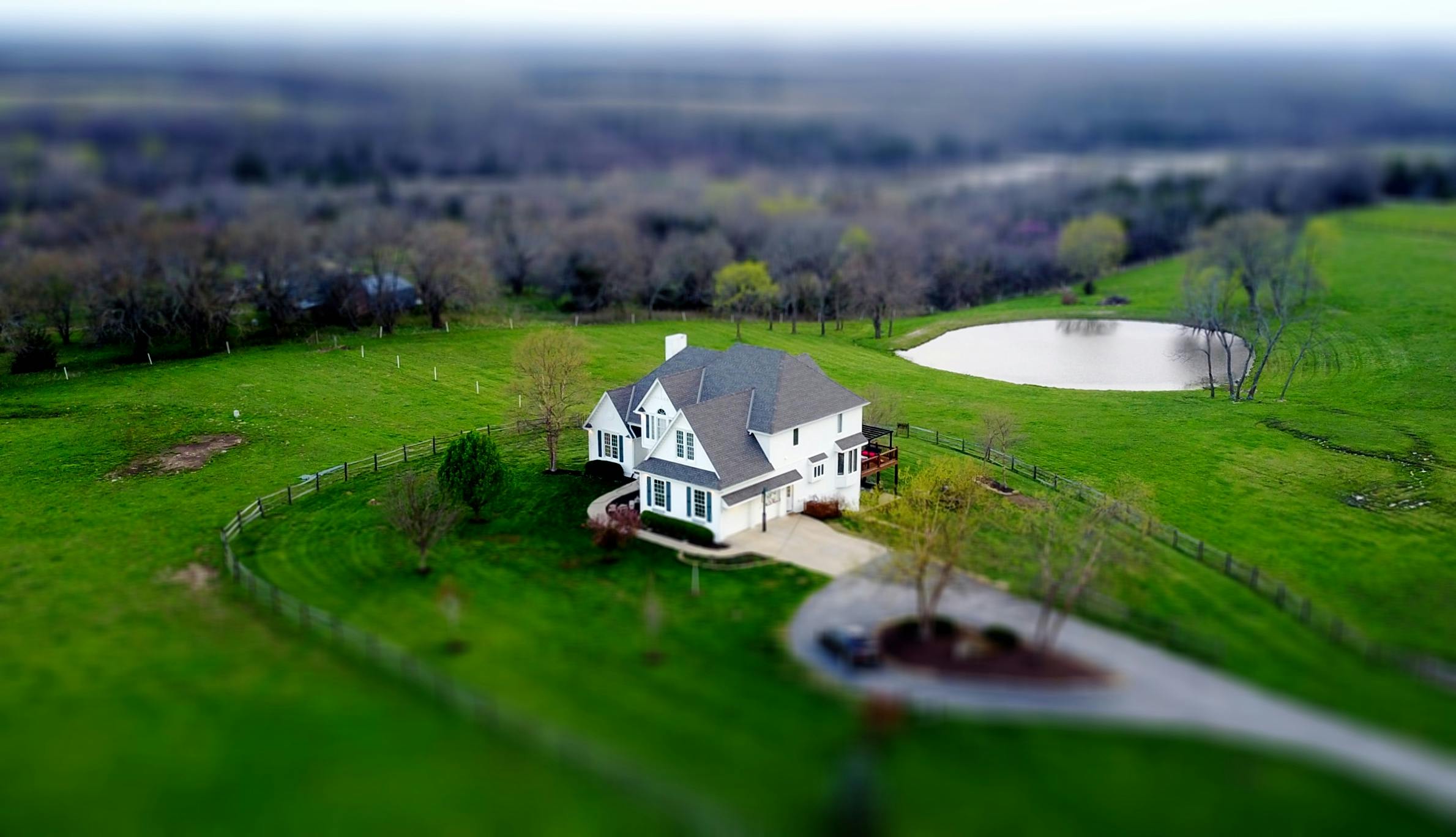 Aerial shot of a charming rural home surrounded by lush green fields and a tranquil pond.